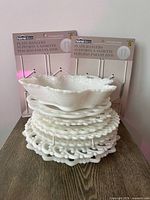 Stack of seven milk glass plates with ruffled handled bowl on top; two packaged plate hanger sets visible