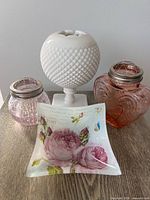 Group shot of all four items on table: white milk glass rose bowl, two pink jars with frog lids, floral trinket dish