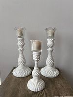Front view of three milk glass hobnail candlesticks with clear glass peg inserts and candles