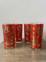 Set of four red and gold paisley highball glasses on tabletop
