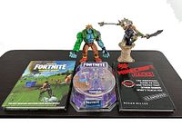 Group shot showing two hardcover books, sealed Teknique figure, loose Darkstalkers figure, and Spawn female warrior statue