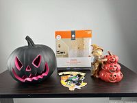 All four items on table: plastic lighted pumpkin, boxed cobweb lights, hanging sign, ceramic figurine