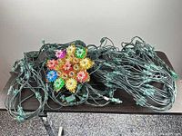 Two green-cord net light strings and multicolor starburst tree topper displayed on table
