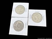 Obverse sides of three 1976 Kennedy half dollars in white cardboard flips