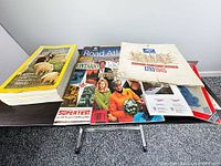 Overall lot on table: National Geographic stack, Rand McNally atlas, People magazine, medals poster, Ontario map