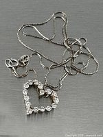 Necklace coiled showing lobster clasp, box chain and heart pendant with clear stones
