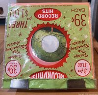 Front view of sealed 7" single in "Last Months Record Hits" poly bag, apple label visible