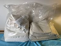 Two clear plastic bags filled with folded white/off-white fabric