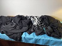 Multiple black fabrics piled, showing different textures including patterned pile and knits