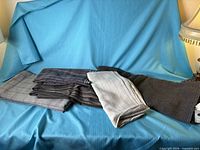 Group of six folded plaid and tweed fabric pieces on blue backdrop