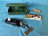 All items: buttonholer, open green case, templates box, booklet, metal pieces