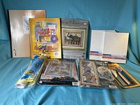 Overall view of lot showing scrapbook, canvases, cross-stitch kits, sketchbook, adhesive film