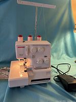 Front view of Janome serger with pedal, thread cones and booklet visible