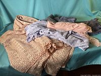 Pile of assorted fabrics showing coral lace, light blue stripe, blush chiffon, grey embroidered, navy lace on aqua backdrop