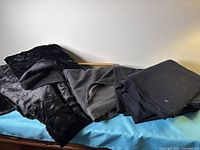 All four folded fabric pieces on table: black faux fur, grey woven, two black fabrics