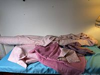 All fabric pieces on bed: rolled tweed bolt, pale pink, dusty rose, floral, textured weave and remnants