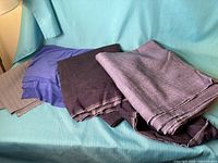 Stack of various folded fabrics showing purple woven, purple stretch, and grey pieces