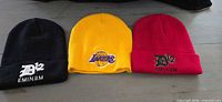 Three knit beanies laid flat showing colors and embroidered logos