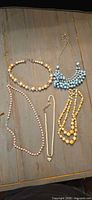 All five beaded costume necklaces arranged on surface showing colors, bead sizes and clasp styles