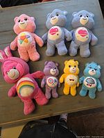 Front view of 8 Care Bears plush toys showing colours and belly badges