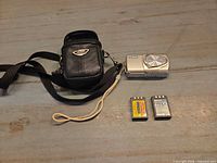 Camera, pouch, two batteries displayed on surface