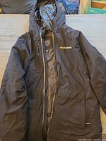 Full front view of black Stormtech coat showing hood, zipper, PaulDavis logo and pockets