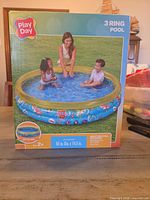Front of retail box showing Play Day 3 Ring Pool with children, brand and product details visible