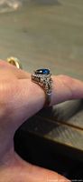 Side view of ring on finger showing blue center stone, halo, and band detail