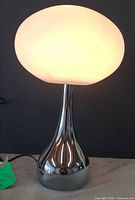 Front view showing entire lit lamp with glass shade and chrome base