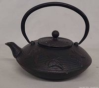 Side view of black cast iron tetsubin with handle, lid, spout, butterfly motif visible