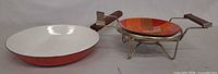 Side view of enamel frying pan beside ceramic mosaic bowl on stand