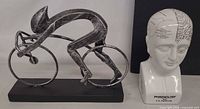 Front view of metal cyclist sculpture alongside ceramic phrenology head bank