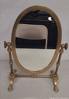 Front view of brass oval tilting vanity mirror on footed stand