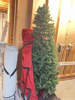 Tree partially inserted in red storage bag showing foliage and bag