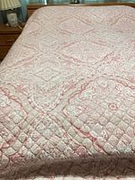 Pink and white quilted paisley bedspread laid on queen bed