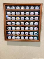 Front view of wood display case showing seven shelves filled with 49 logo golf balls, glass door closed