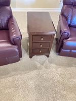Front view of dark brown wood side table showing three drawers and brass knobs
