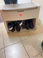 Front view of beige Step2 plastic storage bench with open cubby and shoes inside for scale
