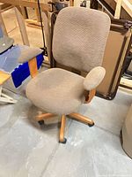 Front view of tan upholstered swivel desk chair showing seat, back, armrests, wood base and casters