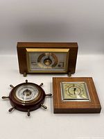 All three wooden tabletop barometers: rectangular Airguide weather station, circular ship-wheel Gischard, square German aneroid