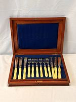 Open mahogany box displaying 6 knives and 6 forks in blue velvet slots
