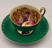 Teacup on saucer, showing interior fruit scene and green exterior