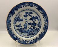 Front view showing entire blue and white porcelain plate with scenic center and decorative border