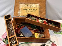 Open wooden box showing assorted Meccano parts and instruction booklet