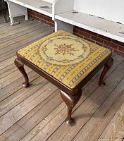 Overall view of bench showing needlepoint top and wooden legs