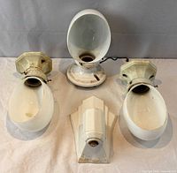 Overall view of the three porcelain wall sconces and their milk glass shades laid out on a cloth