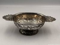 Three-quarter view showing interior repousse scene and both handles