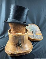 Top hat on wooden form atop leather case with lid leaning