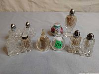 Front view of all ten shakers showing glass patterns, metal lids, porcelain floral single and dome-shaped pair