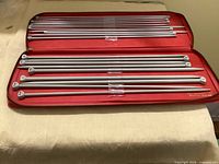 Open red zippered case displaying multiple pairs of grey aluminium knitting needles
